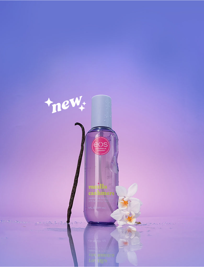 Bottle of EOS Vanilla Cashmere body mist with a vanilla bean and orchid flower on a purple background